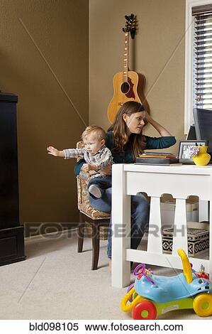 Stock Photography - Caucasian mother using laptop and holding baby. Fotosearch