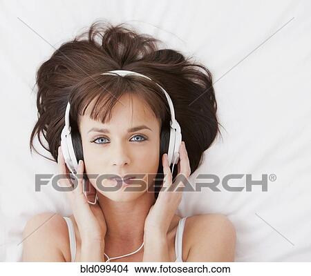 Picture - Caucasian woman in bed listening to music on headphones. Fotosearch