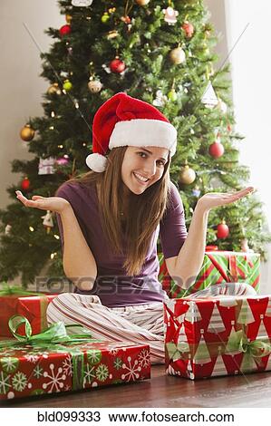 Stock Image - Caucasian woman in Santa hat sitting with Christmas gifts. Fotosearch