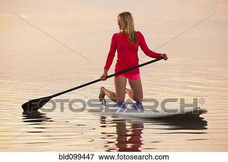 Stock Photo - Caucasian woman kneeling on paddle board. Fotosearch