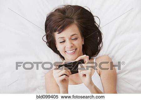 Stock Photography - Caucasian woman laying in bed text messaging on cell phone. Fotosearch