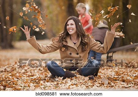Stock Image - Caucasian woman playing in autumn leaves. Fotosearch