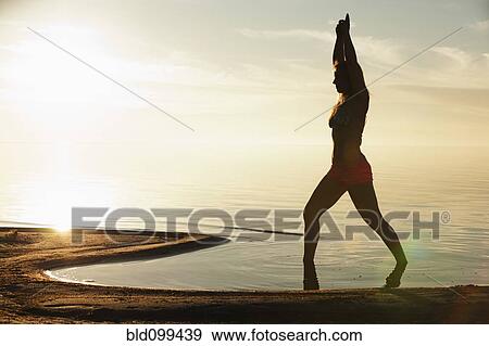Stock Photo - Caucasian woman practicing yoga on beach. Fotosearch