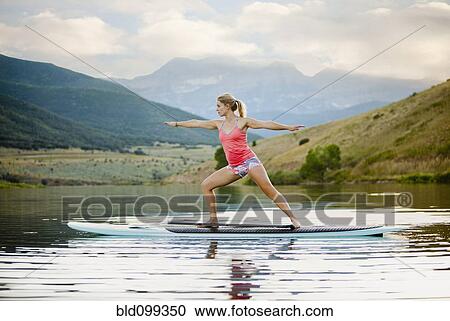 Stock Image - Caucasian woman practicing yoga on paddle board. Fotosearch