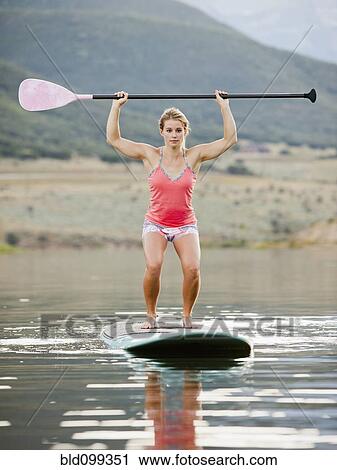 Stock Image - Caucasian woman practicing yoga on paddle board. Fotosearch