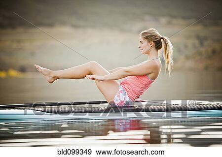 Stock Photo - Caucasian woman practicing yoga on paddle board. Fotosearch