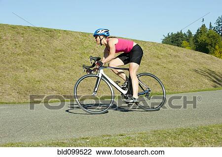 Stock Image - Caucasian woman riding bicycle in park. Fotosearch