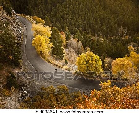 Stock Image - Caucasian woman running along autumn road. Fotosearch