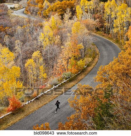 Stock Image - Caucasian woman running along autumn road. Fotosearch