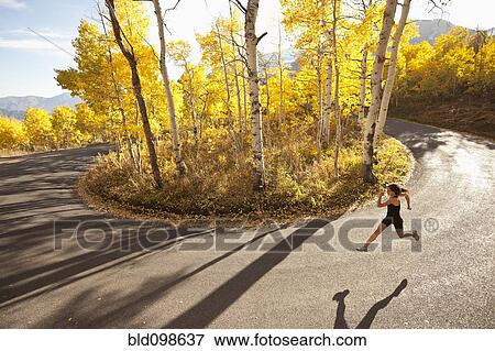 Stock Photo - Caucasian woman running along autumn road. Fotosearch