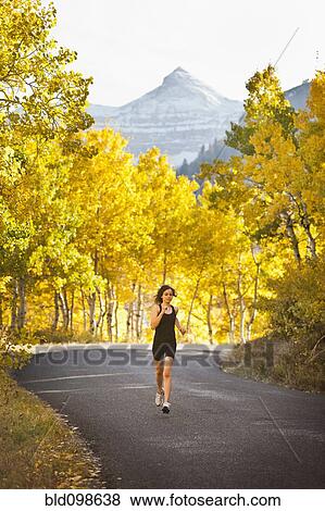 Stock Photo - Caucasian woman running along autumn road. Fotosearch