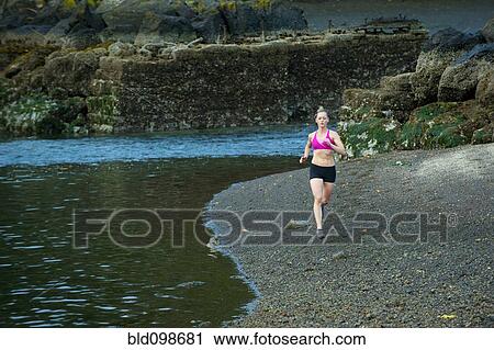Stock Image - Caucasian woman running near lake. Fotosearch