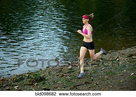 Stock Image - Caucasian woman running near lake. Fotosearch