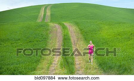 Picture - Caucasian woman running on path through field. Fotosearch