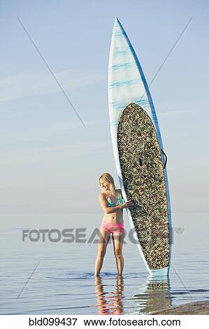Stock Photo - Caucasian woman standing on beach with paddle board. Fotosearch