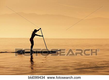 Picture - Caucasian woman standing on paddle board. Fotosearch