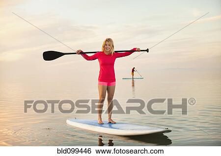 Stock Photograph - Caucasian woman standing on paddle board. Fotosearch