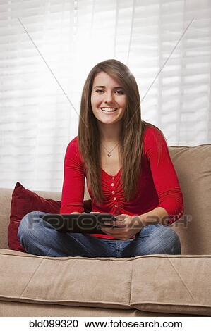Stock Image - Caucasian woman using digital tablet on sofa. Fotosearch