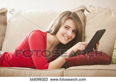 Stock Image - Caucasian woman using digital tablet on sofa. Fotosearch