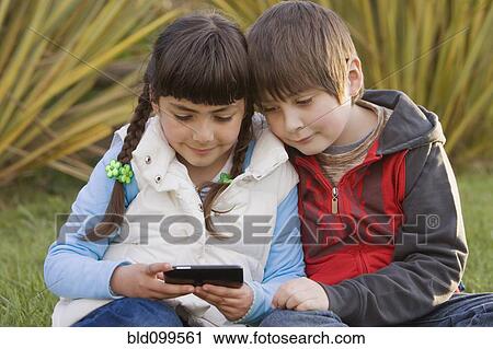 Stock Image - Chilean brother and sister looking at cell phone. Fotosearch