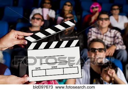 Stock Image - Clapperboard in front of Hispanic people in movie theater. Fotosearch