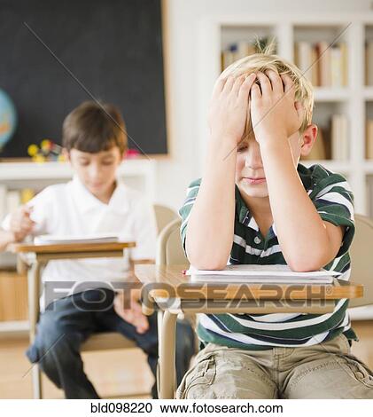 Frustrated Caucasian boy sitting at desk in classroom View Large Photo Image Stock Image - Frustrated Caucasian boy sitting at desk in classroom. Fotosearch