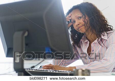 Stock Image - Frustrated Hispanic businesswoman using computer at desk. Fotosearch