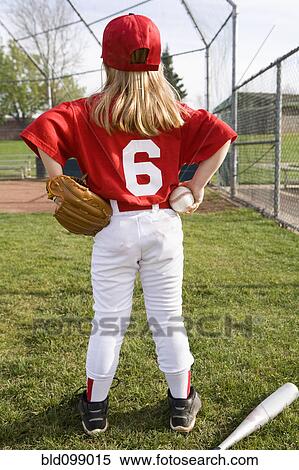 Stock Photography - Girl in baseball uniform standing on field. Fotosearch