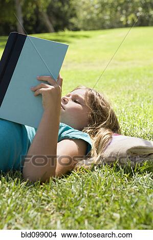 Girl laying in grass reading book View Large Photo Image Picture - Girl laying in grass reading book. Fotosearch