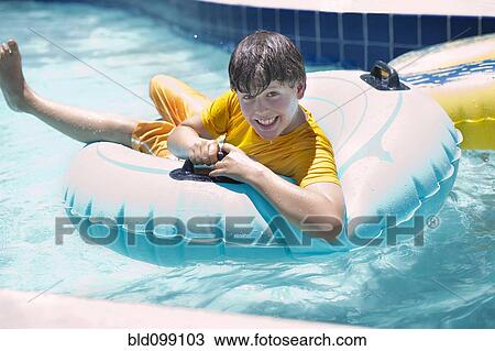 Stock Image - Hispanic boy floating on raft in swimming pool. Fotosearch