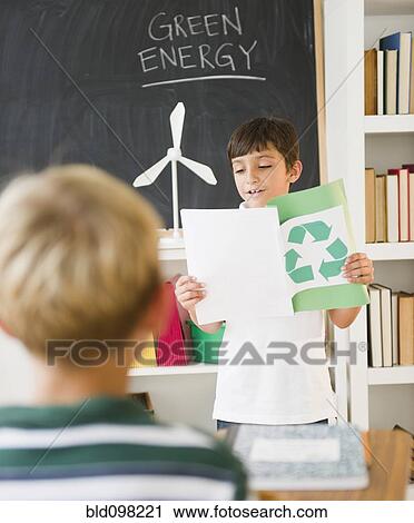 Stock Image - Hispanic boy reading recycling report in classroom. Fotosearch