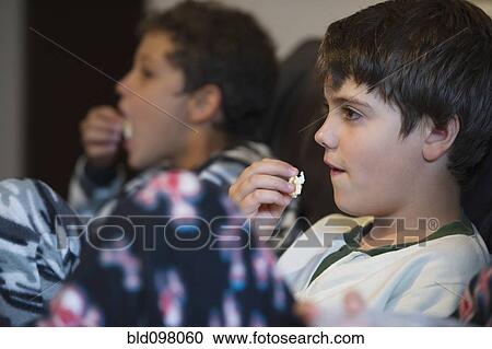 Stock Image - Hispanic boys eating popcorn and watching television. Fotosearch