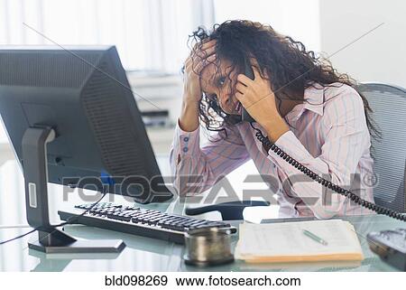 Stock Photo - Hispanic businesswoman talking on telephone at desk. Fotosearch