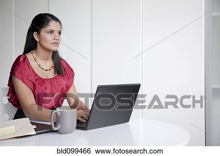 Stock Photograph - Hispanic businesswoman typing on laptop in office. Fotosearch