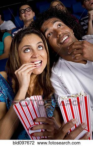 Stock Image - Hispanic couple enjoying popcorn in movie theater. Fotosearch
