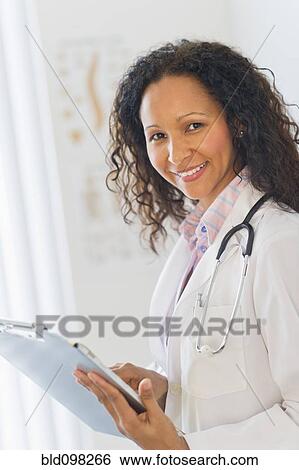 Hispanic doctor looking at medical chart in hospital View Large Photo Image Stock Photograph - Hispanic doctor looking at medical chart in hospital. Fotosearch