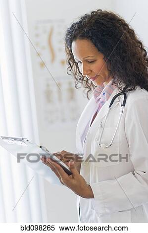 Stock Photography - Hispanic doctor looking at medical chart in hospital. Fotosearch