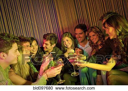 Stock Image - Hispanic friends drinking cocktails in bar. Fotosearch