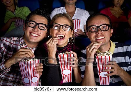 Stock Image - Hispanic friends enjoying popcorn at movie theater. Fotosearch