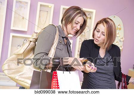 Stock Photo - Hispanic friends looking at jewelry in store. Fotosearch