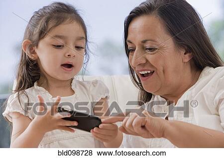 Stock Photo - Hispanic grandmother showing cell phone to granddaughter. Fotosearch
