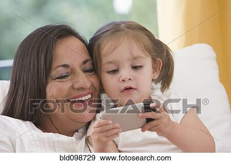 Stock Photo - Hispanic grandmother showing cell phone to granddaughter. Fotosearch