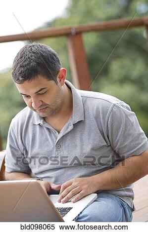 Stock Photography - Hispanic man using laptop outdoors. Fotosearch