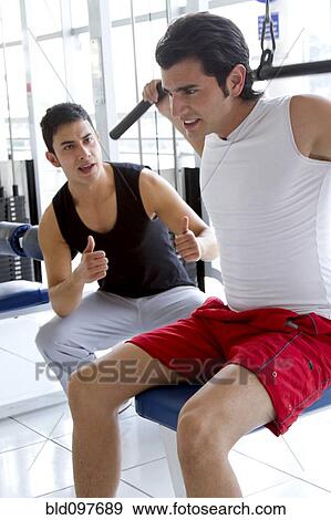 Stock Photo - Hispanic man working with personal trainer in health club. Fotosearch