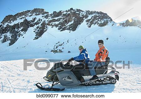 Stock Photo - Hispanic men riding snowmobile together. Fotosearch