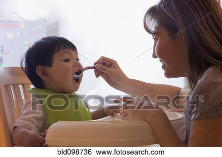 Stock Photograph - Hispanic mother feeding baby boy. Fotosearch