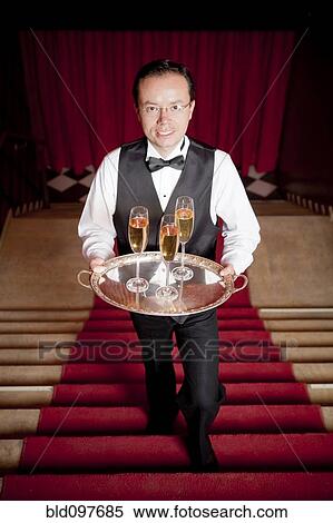Stock Photography - Hispanic waiter climbing stairs carrying Champagne. Fotosearch