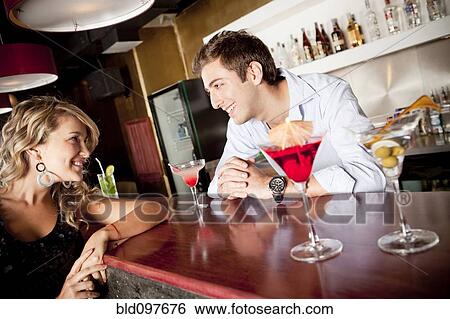 Stock Photograph - Hispanic woman drinking cocktail talking to bartender. Fotosearch