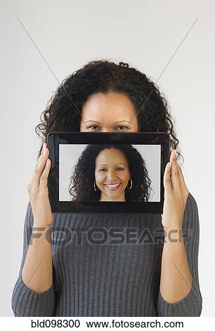 Stock Image - Hispanic woman holding digital tablet in front of face. Fotosearch