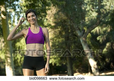 Stock Image - Hispanic woman in sportswear standing in park. Fotosearch